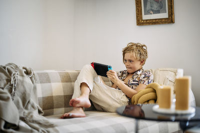 Boy on sofa using digital tablet barefoot