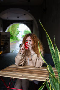 Young red-haired woman alone drinking a drink in a terrace cafe on a rainy day