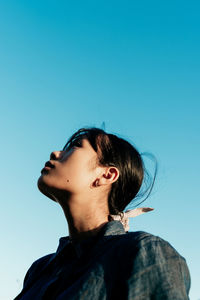 Portrait of young woman looking away against clear blue sky