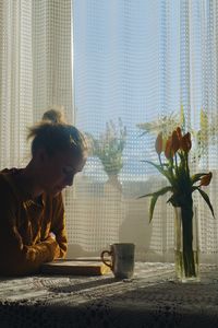 Young woman reading book while sitting at table in house