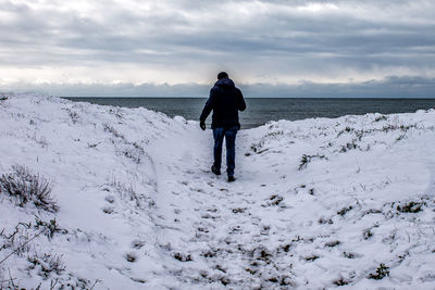 Rear view of man standing on snow covered shore against sky