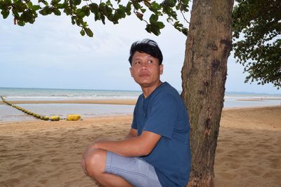 Man crouching by tree at beach