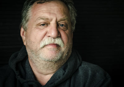 Close-up portrait of senior man against black background