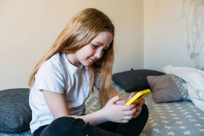 Girl child at home on the couch uses a smartphone