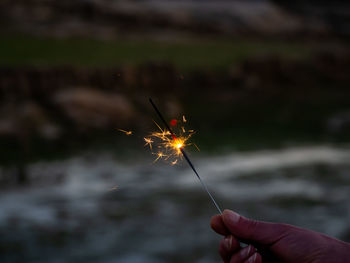 Midsection of person holding sparkler against blurred background