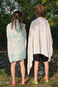 Rear view of friends with towels standing against lake