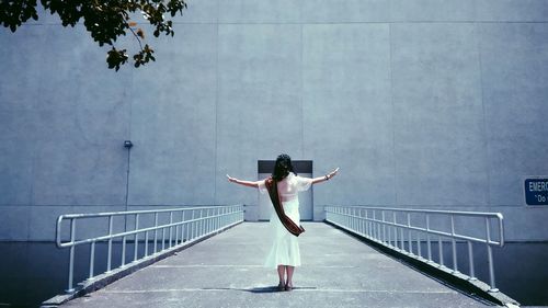 Rear view of man standing on railing against wall