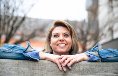 Joyful woman leaning on wooden bench looking upwards with optimism