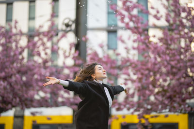 Woman with arms outstretched standing against building in city