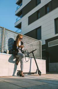 Low angle view of woman using mobile phone while standing on footpath