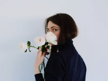 Portrait of beautiful young woman holding flowers against white background