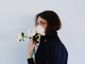 Portrait of beautiful young woman holding rose against white background