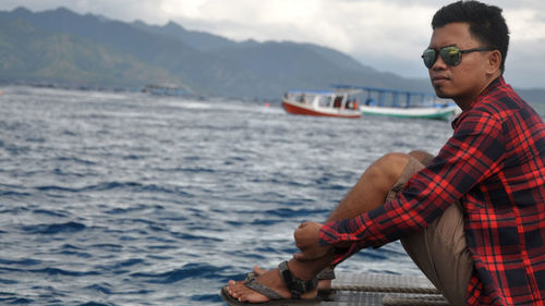 Man sitting on boat in sea against sky