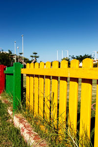 Yellow fence on field against clear blue sky