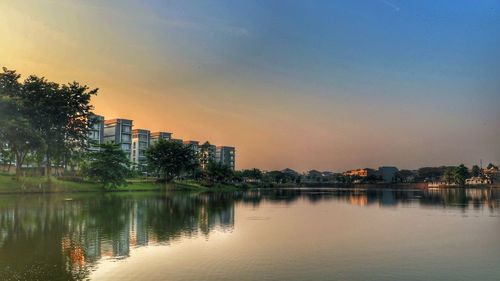 Reflection of buildings in lake against sky at sunset