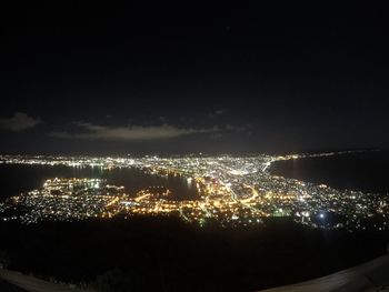 High angle view of illuminated city by sea against sky