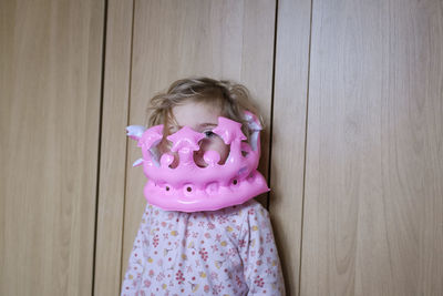 Portrait of cute girl wearing toy crown standing against wall