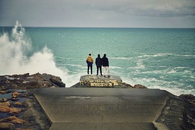 Rear view of men standing on cliff by sea