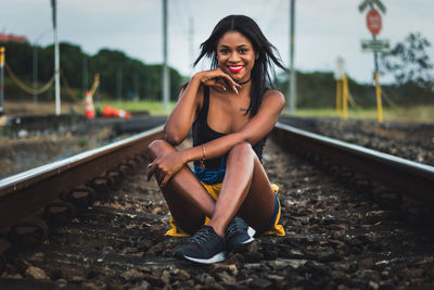 Portrait of smiling young woman sitting on railroad track