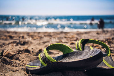 Close-up of shoes on sand at beach against sky