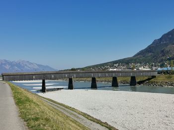 Bridge over lake against clear blue sky