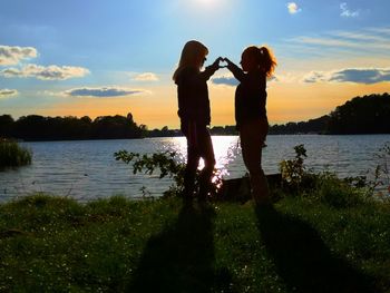 Silhouette woman standing by lake against sky during sunset