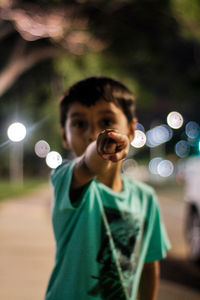 Portrait of boy pointing front while standing outdoors at night