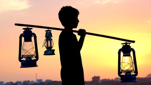 Silhouette man standing by glass against sky during sunset