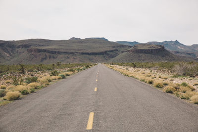 Empty country road passing through arid landscape against sky