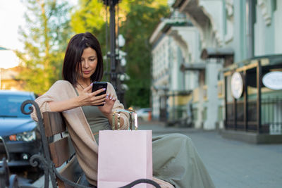 Young beautiful woman smiling going to the shops using smartphone in city