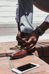 Low section of man tying shoelace on brick wall