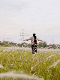 Woman with arms outstretched standing on field against sky