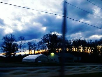 Power lines against cloudy sky at sunset