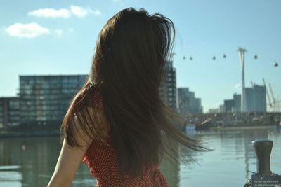 Woman with long hair standing against river in city