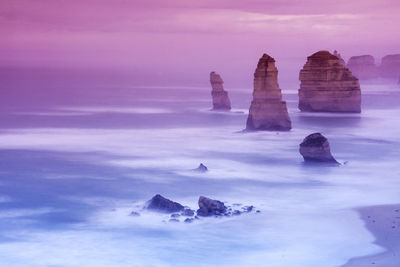 Rock formation in sea against sky during sunrise