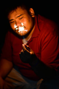 Smiling overweight man holding illuminated sparkler while sitting at night