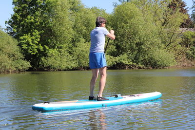 Full length of boy paddleboarding in lake against trees