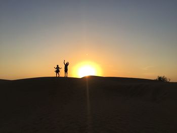 Silhouette people at desert against sky during sunset