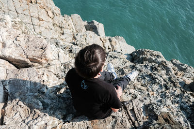 Rear view of woman sitting on rock by sea