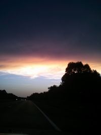 Road amidst silhouette trees against sky at sunset