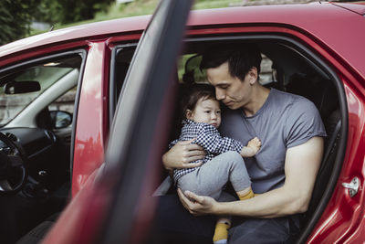 Father carrying male toddler while sitting in car