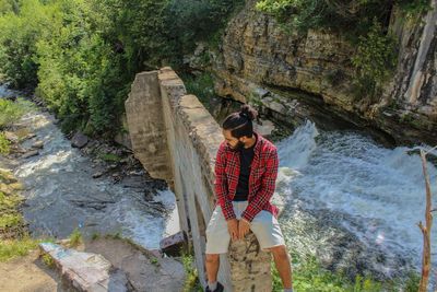 Man sitting on broken wall against stream at forest