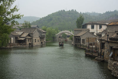 Houses by river and buildings against sky