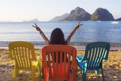 Rear view of woman sitting on chair at beach