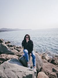 Portrait of man sitting on rock by sea against sky