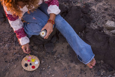 Low section of woman painting stone while sitting on rock