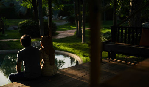 Rear view of a couple sitting at pavilion against trees and river