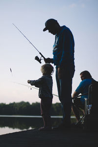 Rear view of men fishing in water against sky