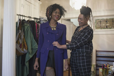 Smiling young woman trying on a coat with her friend