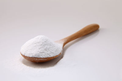 Close-up of baking soda in wooden spoon against white background